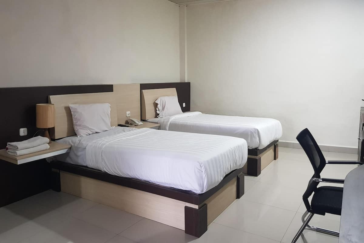 Ein Hotelzimmer mit zwei Einzelbetten, einem Schreibtisch mit Lampe, einem Sessel und einem kleinen Tisch mit Telefon und Buch.