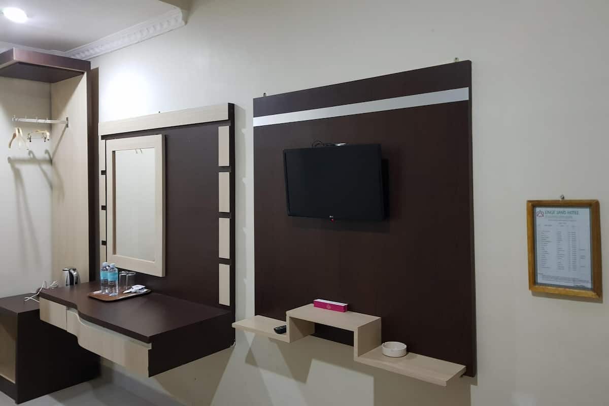 Ein Hotelzimmer mit dunklem Holzschminktisch, einem Spiegel, einem an der Wand befestigten Flachbildfernseher, einem kleinen Regal mit Fernbedienung und einer gerahmten Speisekarte an der Wand.