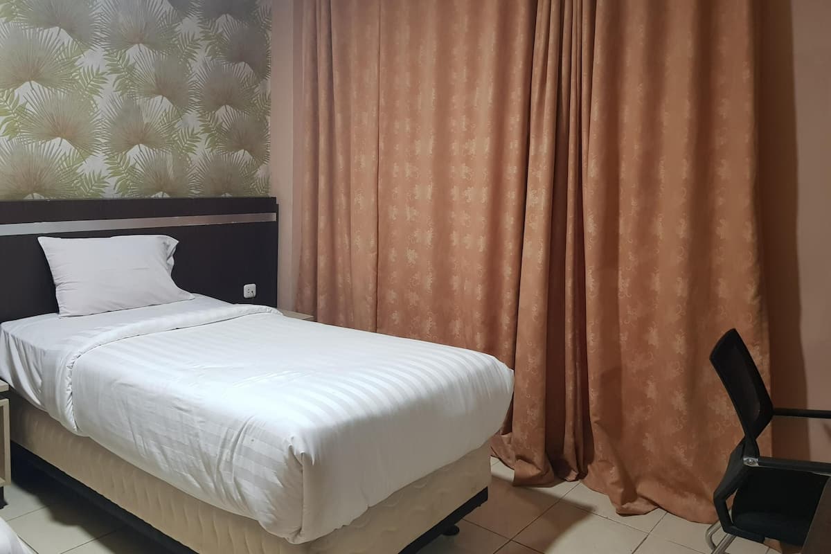 Ein ordentlich bezogenes Bett mit weißer Decke und Kissen, ein Kopfteil, eine Wand mit einem Blattmuster und ein brauner Vorhang.