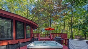 Un jacuzzi en una terraza de madera con barandilla roja, rodeado de árboles.