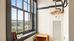 Une pièce d’angle avec une grande fenêtre, un petit tabouret en bois, un radiateur et un porte-manteau.