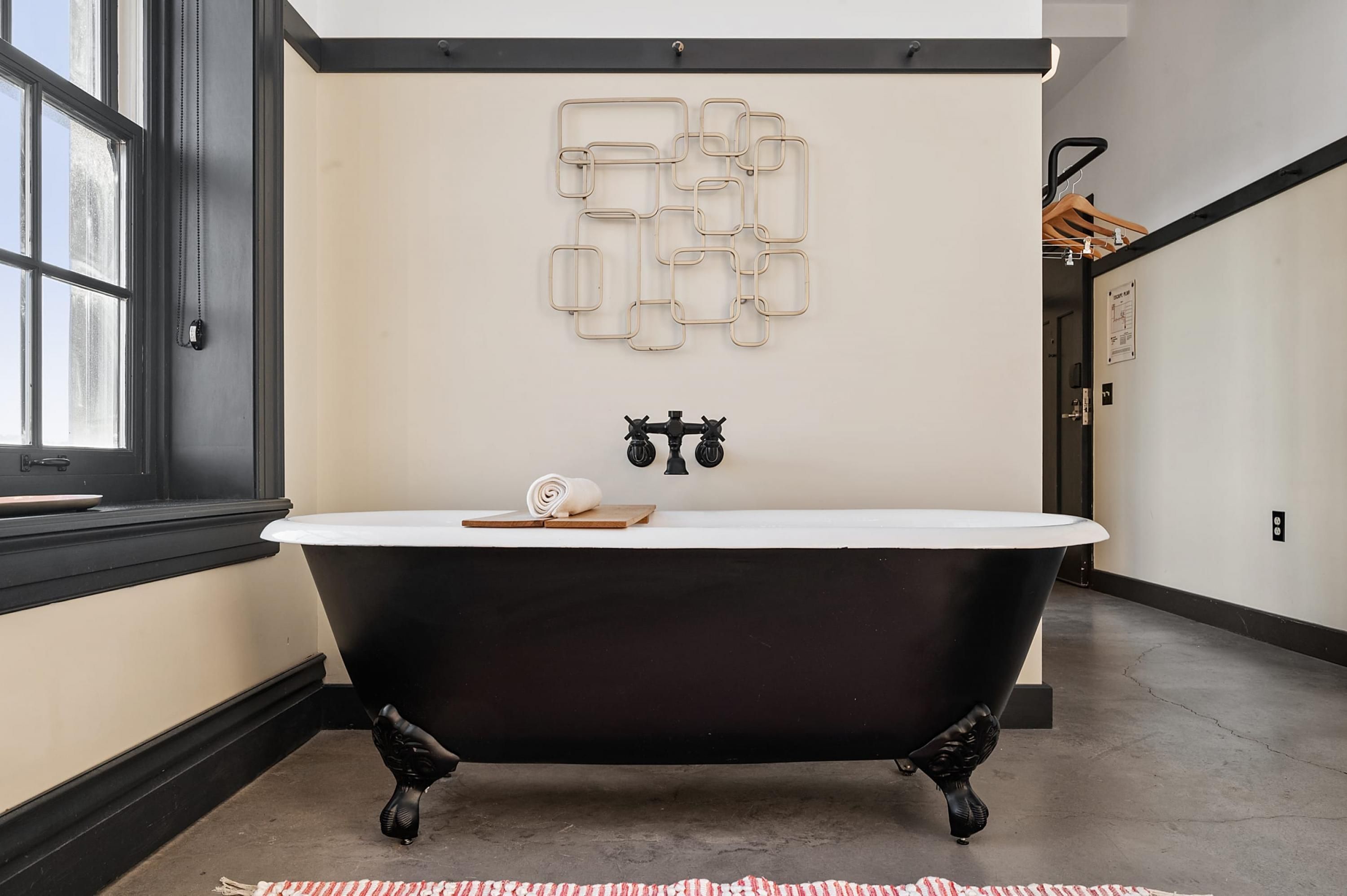 A black clawfoot bathtub with a white interior, a towel, and a wooden tray on a beige wall.