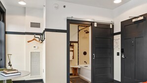 A hotel room with a bed, a desk with chairs, a bathroom with a shower, and a door. - Kasa Trendy Studio Steps to Bakery Square The Maverick (Pittsburgh)