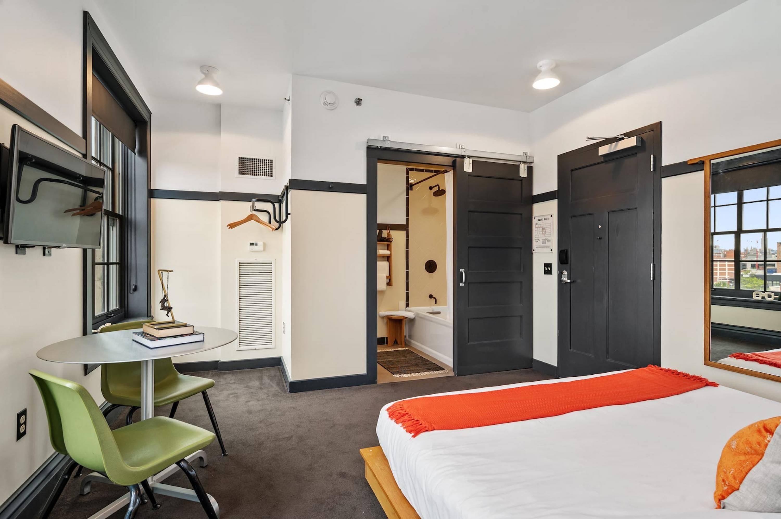 Una habitación de hotel con una cama, un escritorio con silla, un espejo y una ventana.