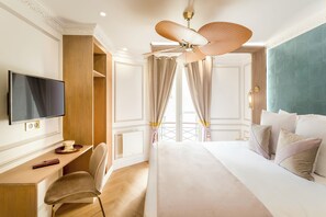A hotel room with a bed, a desk with a TV, a chair, and a ceiling fan.