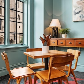 A room with a wooden table and chairs, a lamp, a potted plant, and a view of a building through a window.