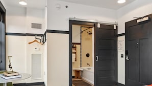 Una camera d'albergo con un letto, una scrivania con sedie, un bagno con doccia e una porta.