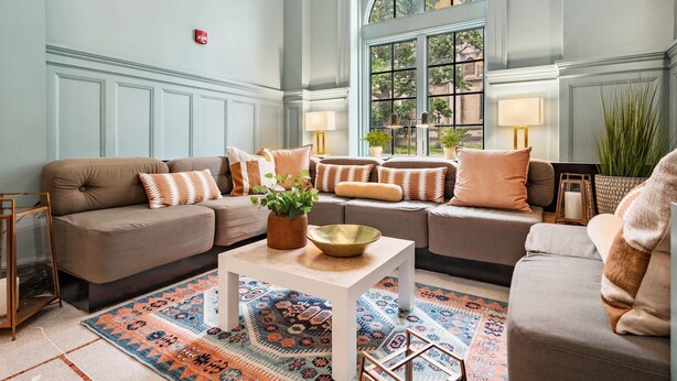 A spacious living room with a large window, a patterned rug, and multiple sofas with decorative pillows.