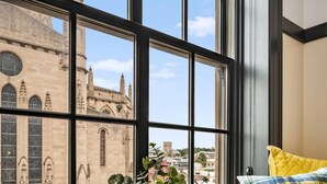 A room with a large window overlooking a historic building, a potted plant, and two plaid pillows.