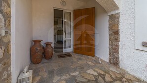 An arched doorway leading to a room with a stone floor, two large vases, and a wooden door with shutters. - Villino la Cicala a Procchio (Marciana)