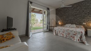 A bedroom with a bed, a TV, a sofa, and a stone wall. - Villino la Cicala a Procchio (Marciana)