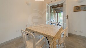 A dining area with a table and chairs, a door leading outside, and a wall-mounted light fixture. - Villino la Cicala a Procchio (Marciana)