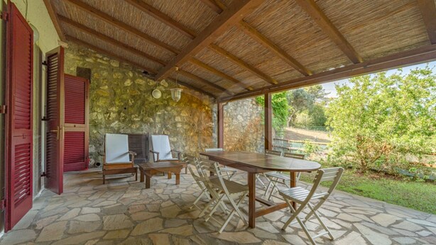An outdoor patio with stone flooring, wooden furniture, and a thatched roof. - Villino la Cicala a Procchio (Marciana)