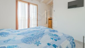 Un dormitorio con una cama, un televisor montado en la pared y un ventanal con cortinas.