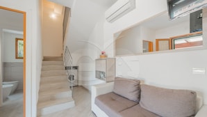 Un interior moderno con una escalera que lleva a un baño, un sofá con cojines y un televisor montado.