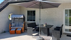 A patio with a table and chairs, a striped lounge chair, and a large umbrella. - Apartment 'Ferienwohnung Neumann' with Private Terrace, Private Garden and Wi-Fi (Neuschoo)