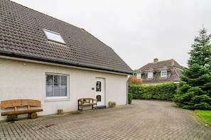 A white brick house with a tiled roof, a wooden bench, and a paved driveway.
