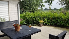 A patio with a table and chairs, a potted plant, and a glass of wine.