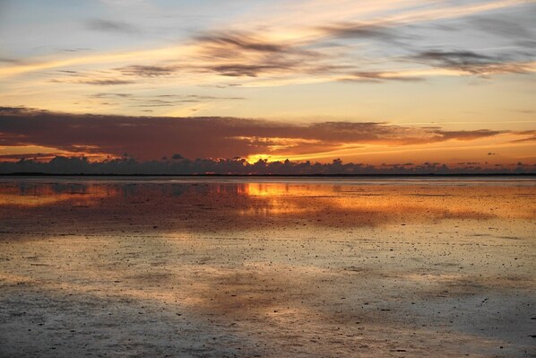 Un coucher de soleil sur une étendue d’eau calme, avec une côte visible au loin.