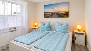 A double bed with matching pillows, two bedside tables with lamps, a window with sheer curtains, and a landscape painting on the wall. - Apartment 'Ferienwohnung Neumann' with Private Terrace, Private Garden and Wi-Fi (Neuschoo)