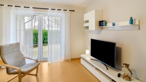 A living room with a television, a chair, a sliding glass door, and a shelf with decorative items. - Apartment 'Ferienwohnung Neumann' with Private Terrace, Private Garden and Wi-Fi (Neuschoo)