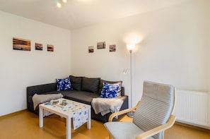 A living room with a sofa, a table, a chair, and wall-mounted artwork.