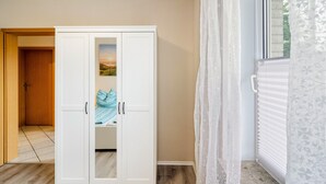 A room with a wardrobe, a bed with a blue blanket, a window with blinds, and a door leading to another room. - Apartment 'Ferienwohnung Neumann' with Private Terrace, Private Garden and Wi-Fi (Neuschoo)