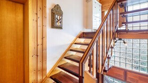 A wooden staircase with a handrail, a wall-mounted mirror, and a window with a view of greenery.