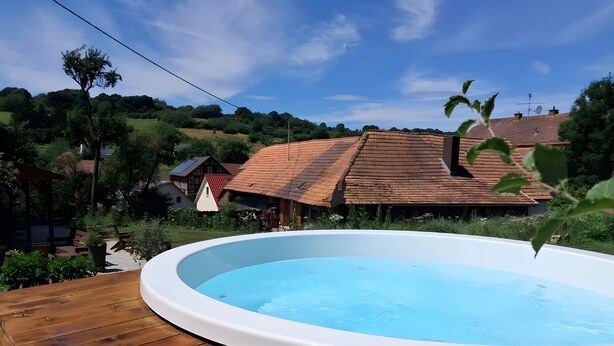 A wooden deck with a hot tub, surrounded by greenery and houses with red roofs.