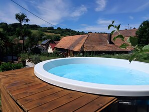 A wooden deck with a hot tub, surrounded by greenery and houses with red roofs. - Holiday Home 'CosyHome Vogelsberg' (Feldatal)