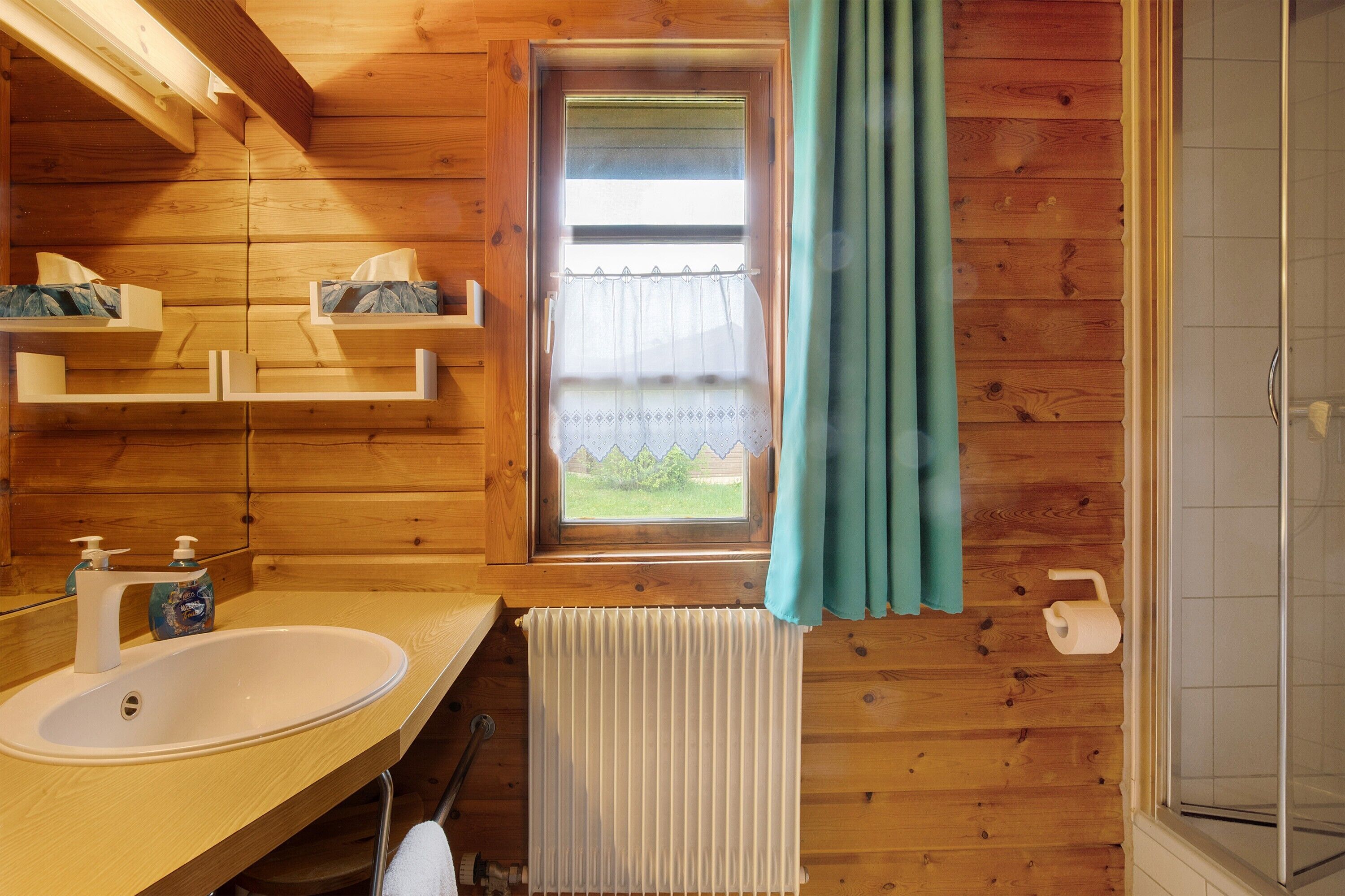 Een houten badkamer met een wastafel, spiegel, raam en douche.