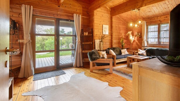 A wooden cabin interior with a large sliding glass door, a sofa set, a dining table, and a fireplace. - Holiday Home 'Hüssli Numero 1' with Private Terrace, Shared Garden and Wi-Fi (Hayingen)