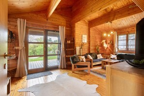 A wooden cabin interior with a large sliding glass door, a sofa set, a dining table, and a fireplace.