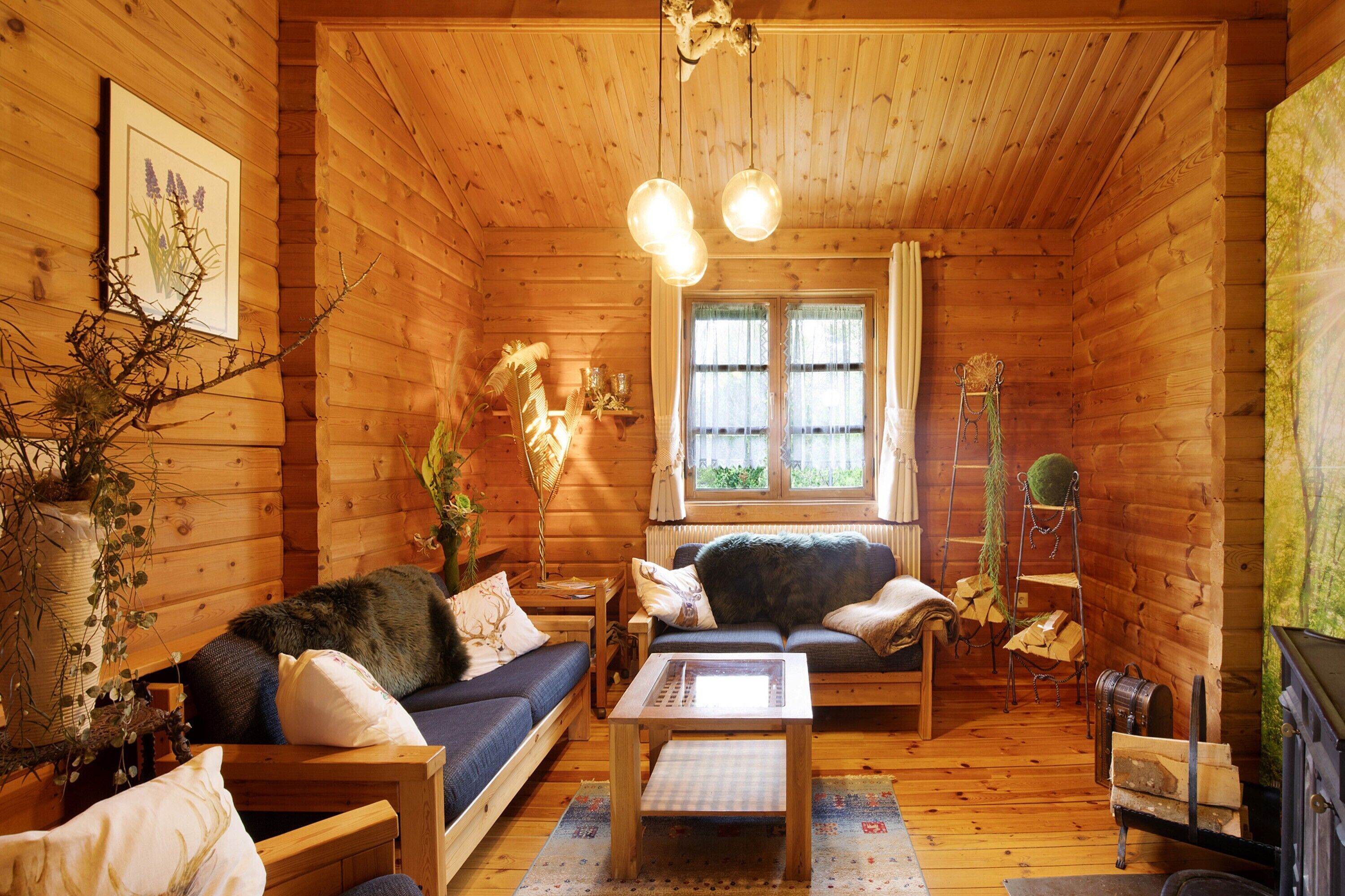 A log cabin interior with a sofa, a table, a fireplace, and a window with curtains.