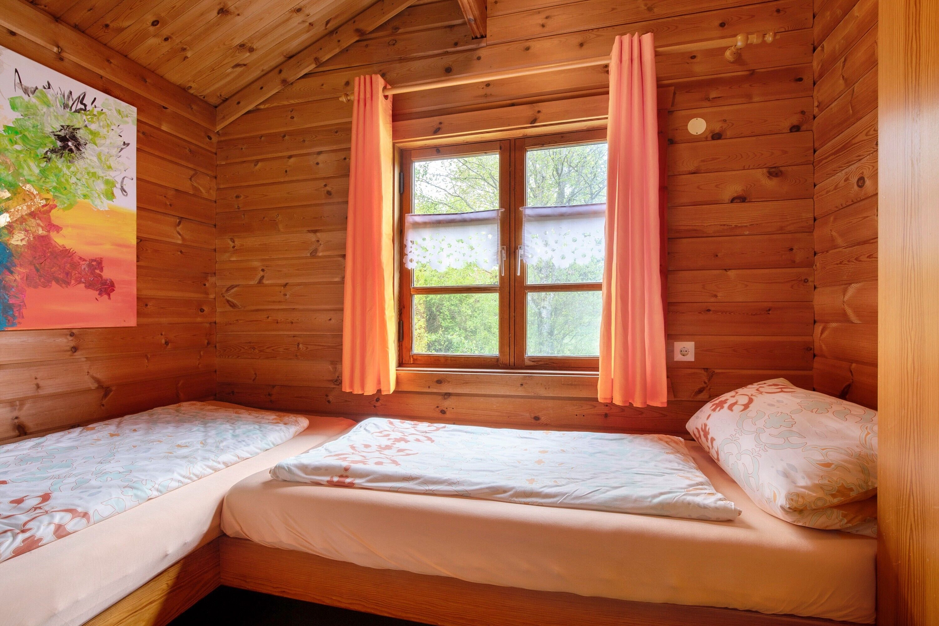 Una cabaña con dos camas de madera, una ventana con cortinas y un cuadro en la pared.