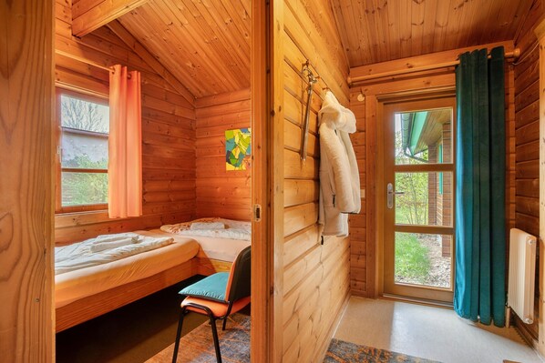 A wooden cabin room with a bed, a chair, a window, and a door.