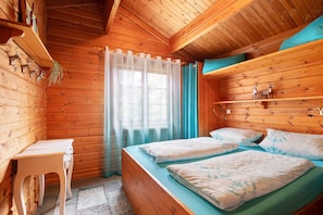 A wooden cabin bedroom with a bed, a small table, and a window with curtains. - Holiday Home 'Hüssli Numero 1' with Private Terrace, Shared Garden and Wi-Fi (Hayingen)