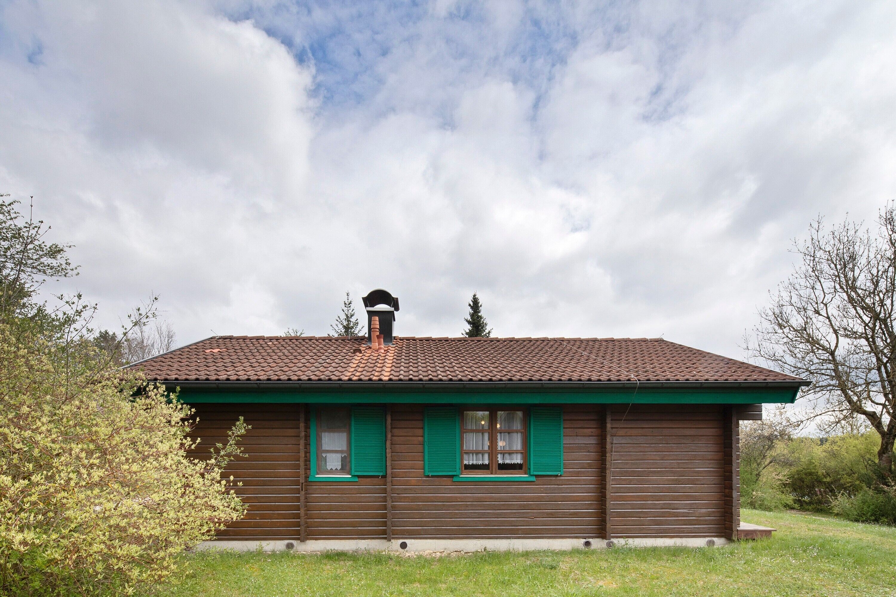 Une maison en bois avec un toit recouvert de tuiles, des volets verts et une cheminée.