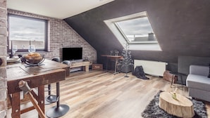 A loft-style living space with a brick wall, wooden flooring, a skylight, a fireplace, a television, a dining table, and a sofa.