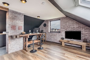 Eine moderne Küche mit Backsteinwand, Holzbarhocker, einer Holzbank und einem an der Wand befestigten Flachbildfernseher.