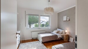 Ein Schlafzimmer mit zwei Betten, einem großen Fenster, einer Heizung und einer weißen Tür.
