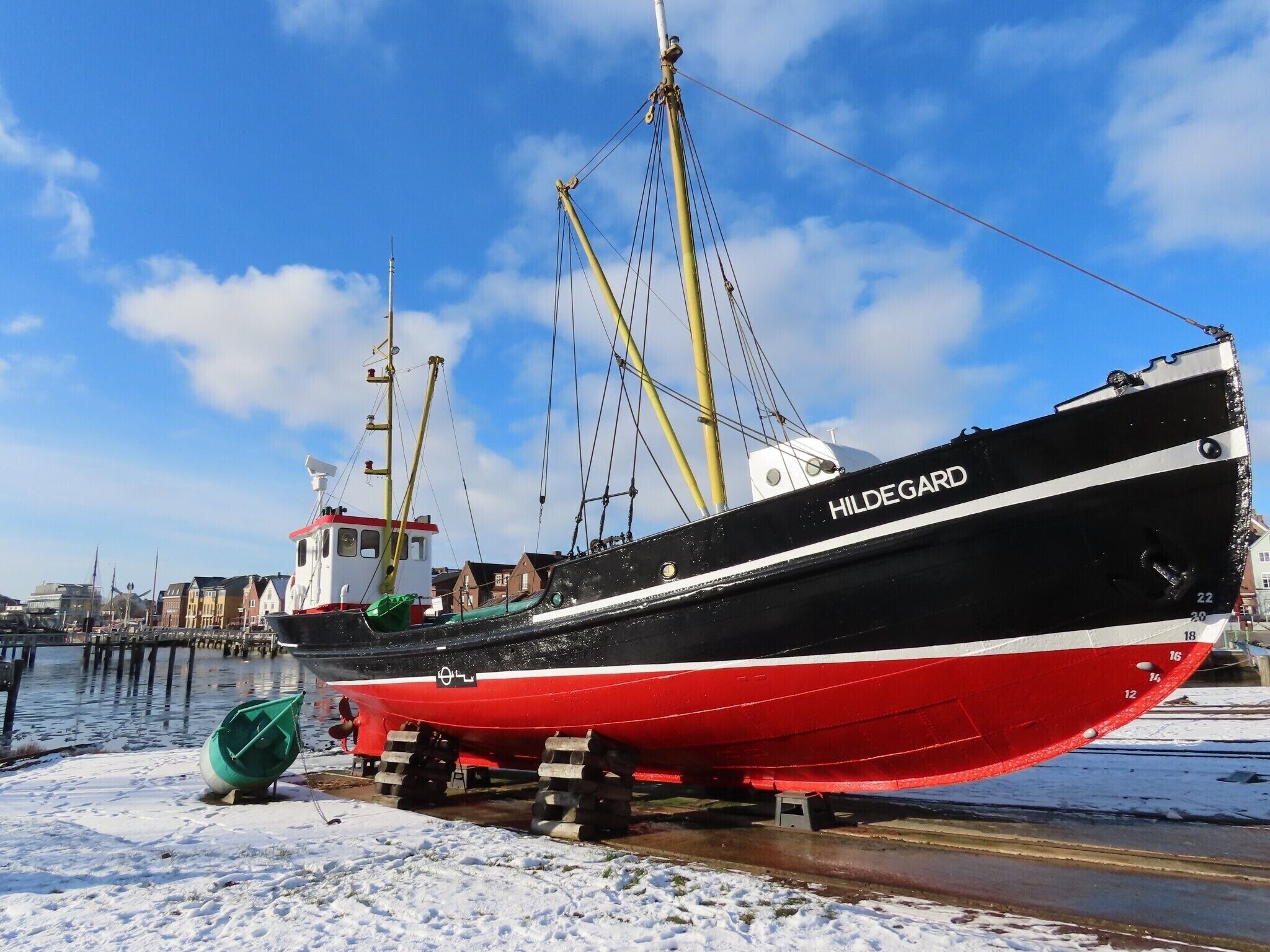A large black and red ship named 'Hildegard' docked at a pier with a clear sky and buildings in the background.