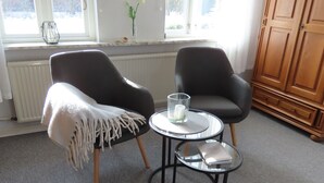 Två stolar med en vit pläd över, ett litet bord med ett ljus och en vas med blommor på en fönsterbräda.