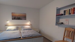 Ett sovrum med en säng, en stol, en bokhylla och en tavla på väggen.
