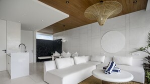 A modern living room with a white sofa, a coffee table, and a kitchen area in the background.