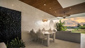 A modern dining area with a stone wall, a round table with chairs, and a view of the landscape.