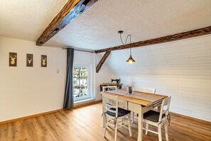 A dining area with a wooden table and chairs, a hanging pendant light, and a window with curtains.
