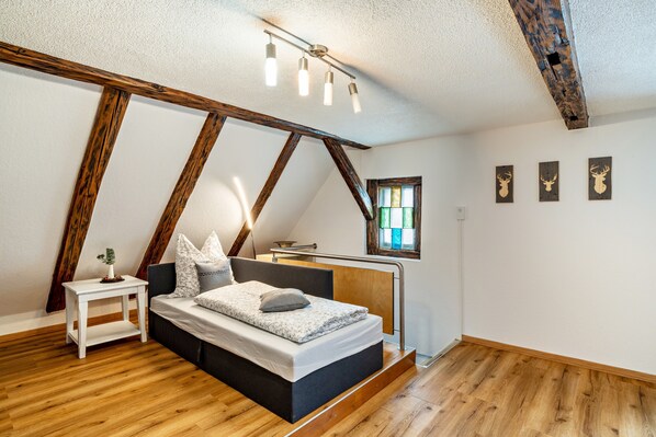 A bedroom with a bed, bedside table, and a window with stained glass.