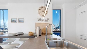 A modern kitchen with a large clock, a 'Welcome' sign, and a view of boats through large windows. - Houseboat 'Sutje' with Sea View, Private Terrace and Wi-Fi (Großenbrode)