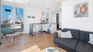 A modern living room with a grey sofa, a small ottoman, and a dining area with bar stools. - Houseboat 'Sutje' with Sea View, Private Terrace and Wi-Fi (Großenbrode)
